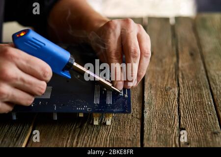 Technician or engineer is focused on repairing electronic circuit board with soldering iron. Man hands soldiers computer circuit board using soldering Stock Photo