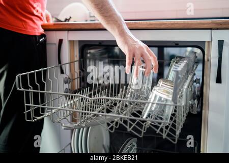 Close up of a Man Loading Dishwasher In Kitchen. Housework Stock Photo