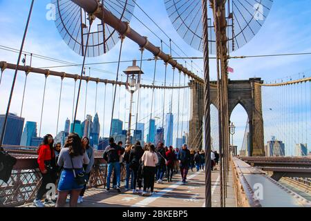 Crossing Brooklyn Bridge with tourists sightseeing and a view of the skyline of Lower Manhattan with the One World Trade Center. Stock Photo