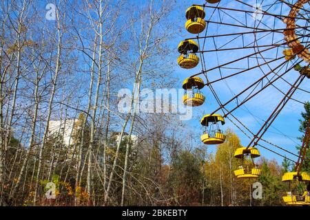 Iconic ferris wheel at the abandoned amusement park of Pripyat, Ukraine, site of the Chernobyl nuclear desaster, and view of the remains of Pripyat. Stock Photo