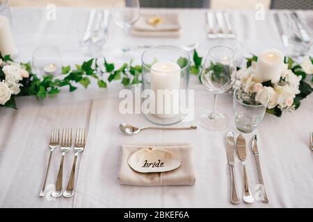 Close-up of a wedding dinner table. The inscription BRIDE on the shell in center of the table. Serving a table - knives, forks, glasses, wine glasses Stock Photo