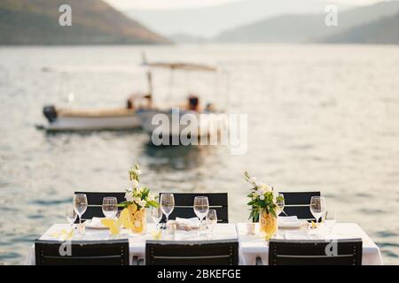 Wedding dinner table reception. Rectangular tables with white tablecloth, floral arrangements lemons in vases. Yellow paper butterflies are scattered Stock Photo