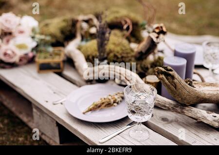 Close-up of a wedding dinner table. A table made of construction pallet decorated with driftwood and a car. The branches of the tree lie among plates Stock Photo