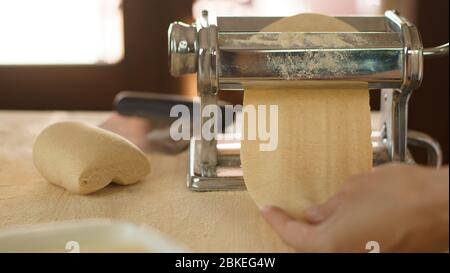 Making fresh homemade pasta: woman's hand pulling out the rolled dough from the manual pasta making machine backlit Stock Photo