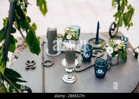 Close-up of a wedding dinner table at reception. Grey thick candles, blue thin candle, small tablet candles in blue glasses burn standing on a metal Stock Photo