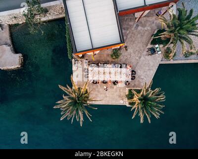 Wedding Reception Table Setting, dinner by the sea aerial top view. Guests at the wedding banquet sit at the table, the photo was taken by a drone.  Stock Photo