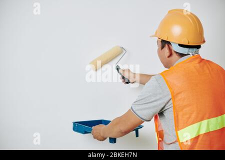 Painter in orange vest and hardhat using tray to catch excess paint when painting house wall Stock Photo