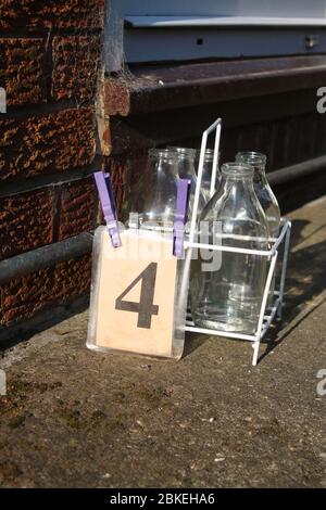 Milk crate on driveway by front door of a house waiting for doorstep milk delivery, with four reusable glass bottles ready for collection by milkman. Stock Photo