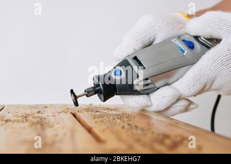 Professional carpenter using rotary hand tool to clean elongated hole in stool or other piece of furniture Stock Photo