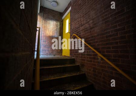 Dark unlit urban stairwell, with yellow door. Stock Photo