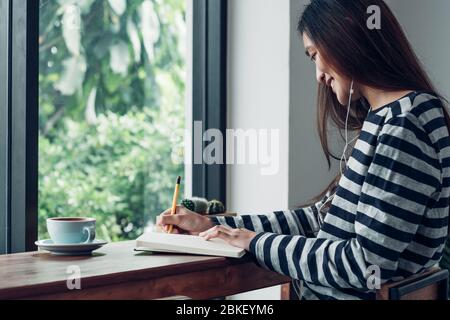 asian woman write plan to do list on notebook white listening music at home in quarantine time Stock Photo