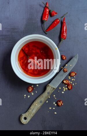 Chili oil in bowl with knife and chili peppers, food photography, studio shot, Germany Stock Photo