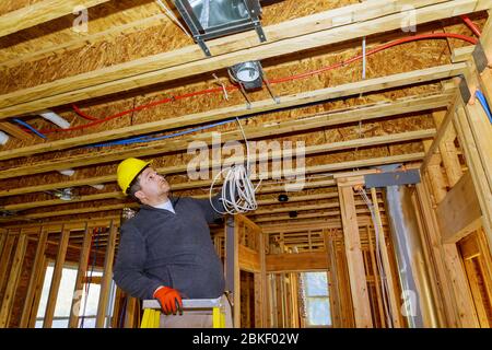 Electrician installing electrical cable wire in new house construction site Stock Photo