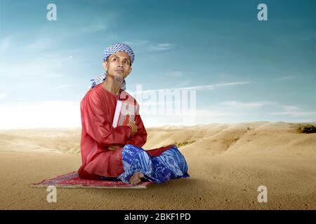 Asian Muslim man sitting and holding the Quran on the desert Stock Photo