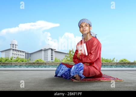 Asian Muslim man sitting and holding the Quran outside the mosque Stock Photo