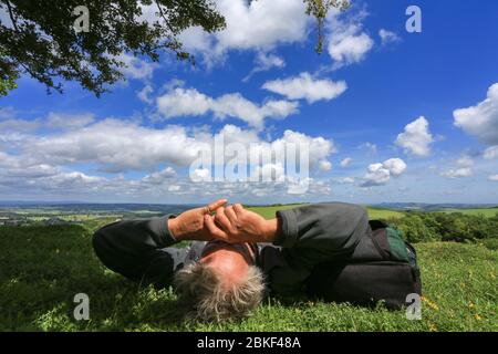 Man relaxing in summer sunshine, lying under a summer sky shielding his eyes with both arms from the sun Stock Photo