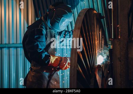 Professional welder performs welding work on metal in protective mask. Industrial concept. Stock Photo