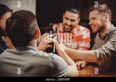 Four bearded young men old friend celebrating, celebrate narrow range in Brasserie, drinking craft beer beverages from bottles, talking toast Stock Photo