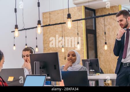 Handsome young executive explaining new employees an online task on theirs computers Stock Photo