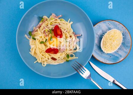 Carbonara pasta - spaghetti with small pieces of bacon, mixed with sauce of eggs, parmesan cheese. Blue plate on a blue background. Macanons with egg Stock Photo