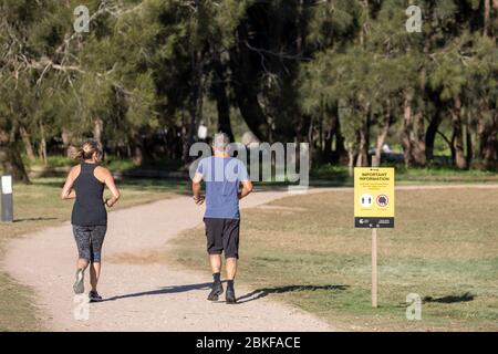Australian man and woman middle aged exercising during covid 19 pandemic jog past a sign reminding of social distancing Stock Photo