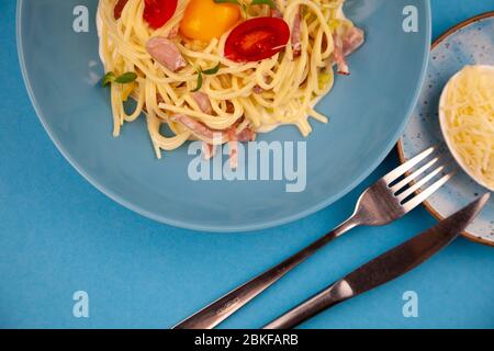 Carbonara pasta - spaghetti with small pieces of bacon, mixed with sauce of eggs, parmesan cheese. Blue plate on a blue background. Macanons with egg Stock Photo
