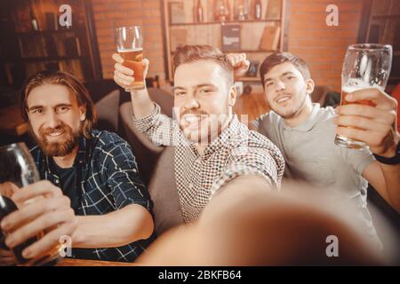Taking selfie with your hand Three bearded friends having fun at bar, posing for photo, looking camera of smartphone. Stock Photo