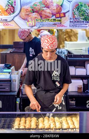 Osaka / Japan - October 1, 2017: Street vendor skillfully preparing local Osaka delicacy takoyaki, ball-shaped Japanese snack made filled with minced Stock Photo