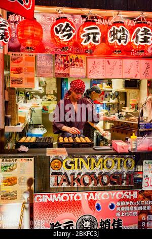 Osaka / Japan - October 14, 2017: Street vendor skillfully preparing local Osaka delicacy takoyaki, ball-shaped Japanese snack made filled with minced Stock Photo