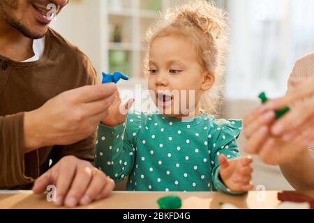 Horizontal medium close up shot of young father demonstrating blue play dough shape to his joyful little daughter Stock Photo