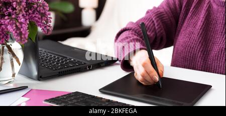 Graphic Designer retoucher freelancer works from home. Woman draws on graphic tablet in home office using laptop and computer. Remote work in cozy hom Stock Photo