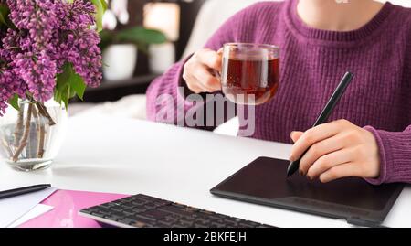 Graphic Designer retoucher freelancer works from home. Woman draws on graphic tablet in home office using laptop and computer. Remote work in cozy Stock Photo