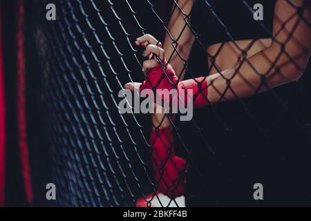 Female fist in bandages for boxing grabs ring grille. Concept of power, feminism, fighting without rules. Stock Photo
