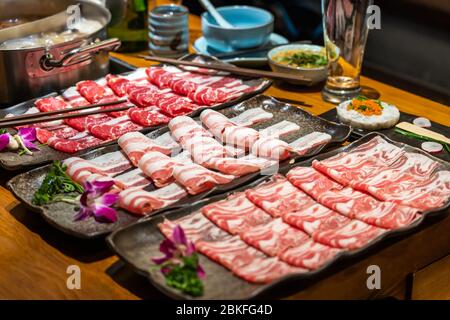 Selection of meat platters to be cooked in hotpot restaurant, including beef, lamb and pork. All thinly sliced for quick cooking. Sauces and pot in ba Stock Photo