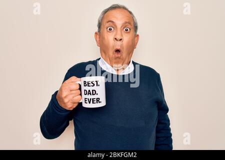 Senior man drinking cup of coffee with best dad ever message over white background scared in shock with a surprise face, afraid and excited with fear Stock Photo
