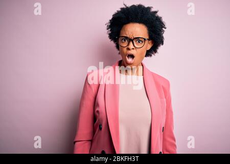 Young beautiful African American afro businesswoman with curly hair wearing pink jacket In shock face, looking skeptical and sarcastic, surprised with Stock Photo
