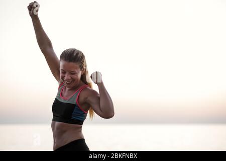 Young woman standing by the sea with arms raised in triumph Stock Photo