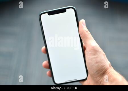 A hand is holding a Apple iPhone X on a plane background. iPhone X has a blank white background on its screen. The picture is shot in Istanbul, Stock Photo