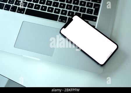 There is an Apple iPhone XS on a MacBook Pro on the office desk. It is common for people using Apple products both for mobile phones and laptops. Stock Photo