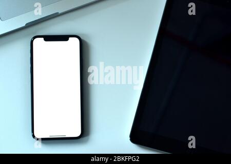 An Apple iPhone XS, a MacBook Pro and  an iPad on the office desk. It is common for people using Apple products both for mobile phones and laptops. Stock Photo