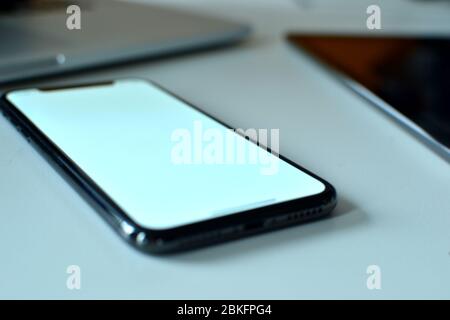 An Apple iPhone XS, a MacBook Pro and  an iPad on the office desk. It is common for people using Apple products both for mobile phones and laptops. Stock Photo