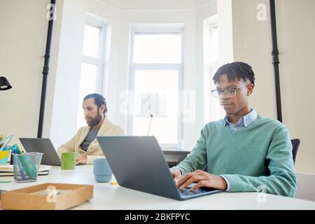 Two young adult managers wearing stylish outfits sitting at table in modern office working on laptops Stock Photo
