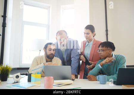 Group of four business people working together on new project looking at statistics on laptop, horizontal shot Stock Photo