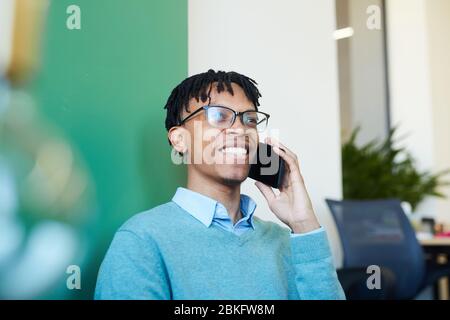 Young African-American male office worker wearing eyeglasses talking on phone with someone and smiling Stock Photo