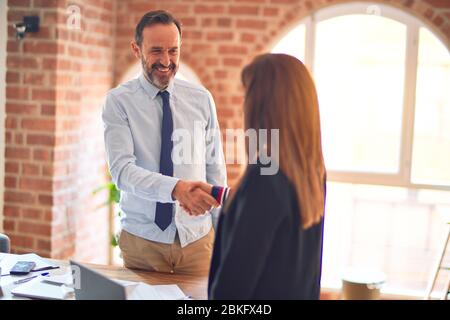 Two middle age business workers smiling happy and confident. Working together with smile on face using laptop doing handsake at the office Stock Photo