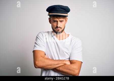 Young driver man with beard wearing hat standing over isolated white background skeptic and nervous, disapproving expression on face with crossed arms Stock Photo