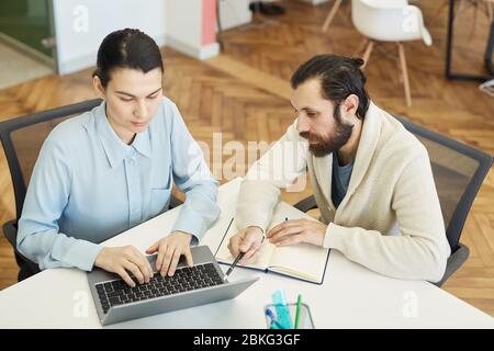 Horizontal high angle shot of two young adult finance managers sitting at office desk working together Stock Photo