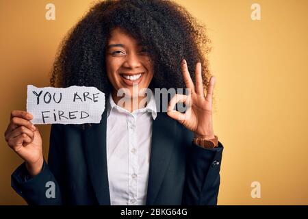 African american business boss woman with afro hair holding you are fired paper for dismissal doing ok sign with fingers, excellent symbol Stock Photo