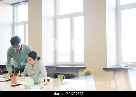 Horizontal shot of young African American man helping his female colleague with work in spacious office room, copy space Stock Photo