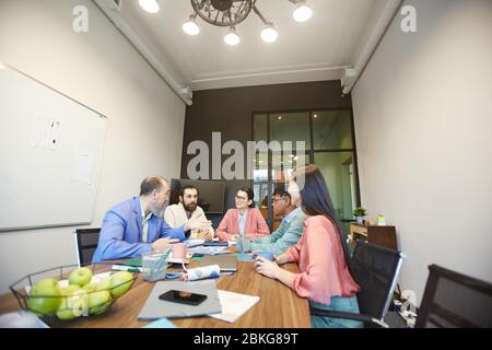 Group of stylish office workers sitting together in modern office board room doing brainstorming, copy space Stock Photo